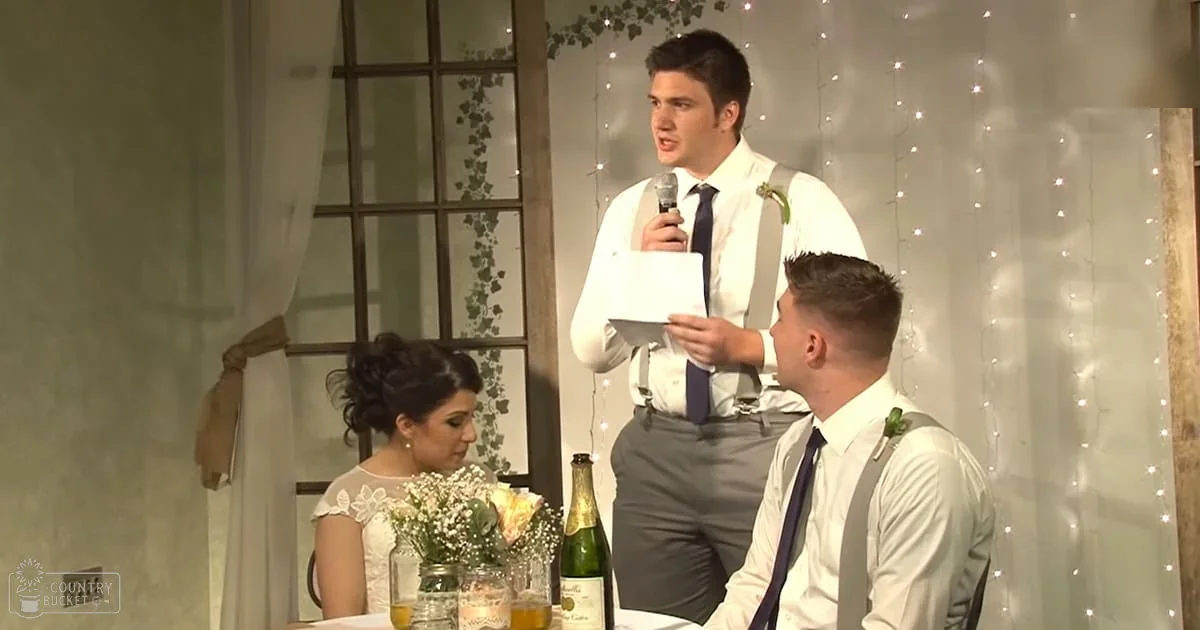 A wedding scene with an adult male singer holding a microphone, another young man seated right, and an adult woman seated left. The setting includes string lights and a bouquet of flowers on the table in what appears to be an indoor venue decorated for a celebratory occasion.