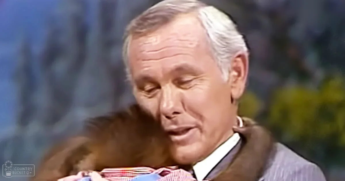 An older adult male interacts with a monkey in a studio setting; the man wears a brown vest over a striped shirt and tie, while the monkey holds what appears to be a colorful object.
