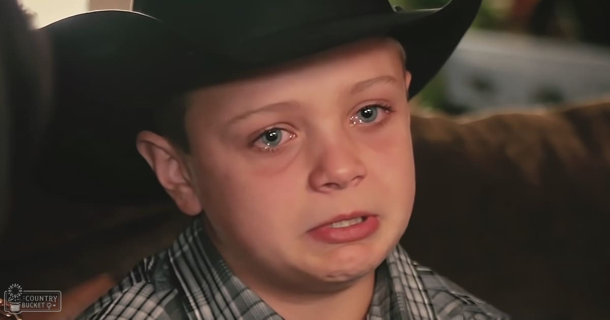 A toddler wearing a green and white plaid shirt indoors in a living room with soft lighting.