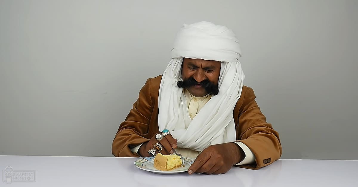 Adult male with mustache, wearing headscarf and jacket in modern indoor setting