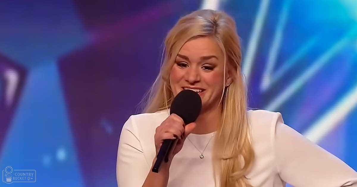 A young adult female wearing a white, long-sleeved, fitted top with modern casual style sings into a microphone at what looks like a talent show or performance setting under vibrant blue and purple lighting.