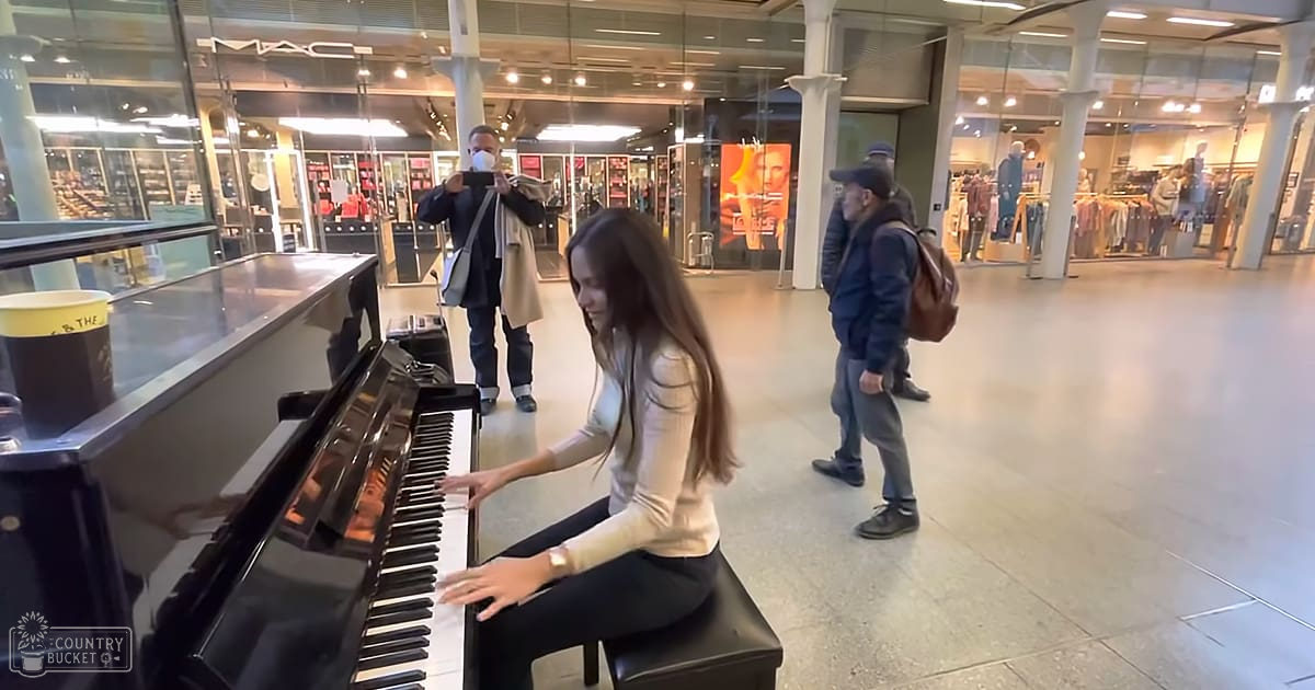 A young adult female playing piano at a MAC cosmetics store in a busy shopping mall, surrounded by adults walking and interacting.