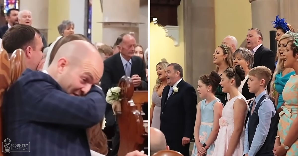 A wedding ceremony inside a church with yellow walls and natural light streaming in. A wooden pew is partially visible on the left side, adorned with a bouquet of white flowers.