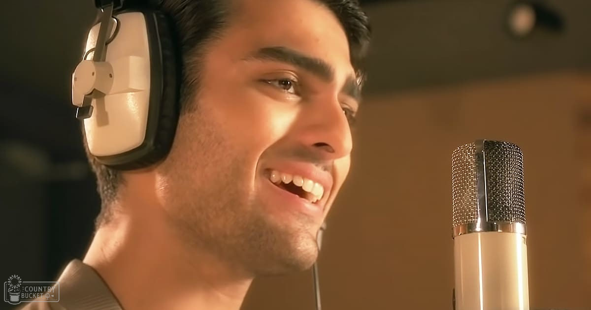 A young adult male in a recording studio, wearing a modern casual beige collared shirt with long sleeves. The setting includes soundproofing panels on the wall and professional microphone in focus.
