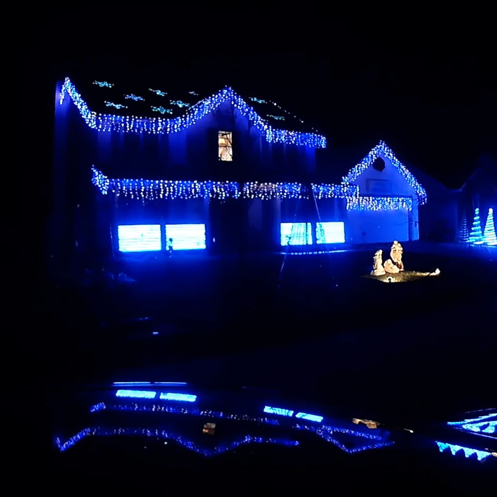 A house adorned with numerous blue string lights at night, creating a festive atmosphere; windows display white light displays inside.