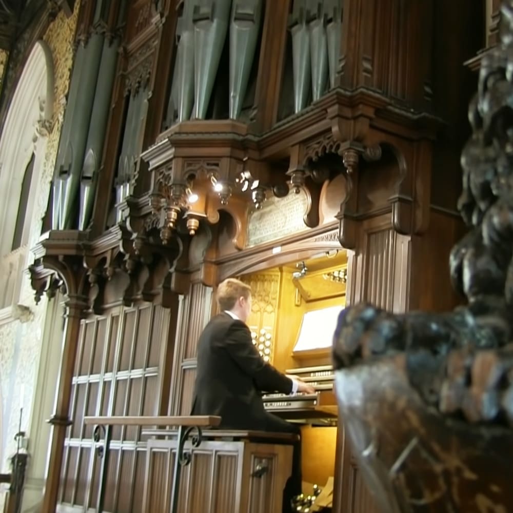 A young adult male playing an organ in a church or cathedral with warm, ambient lighting.