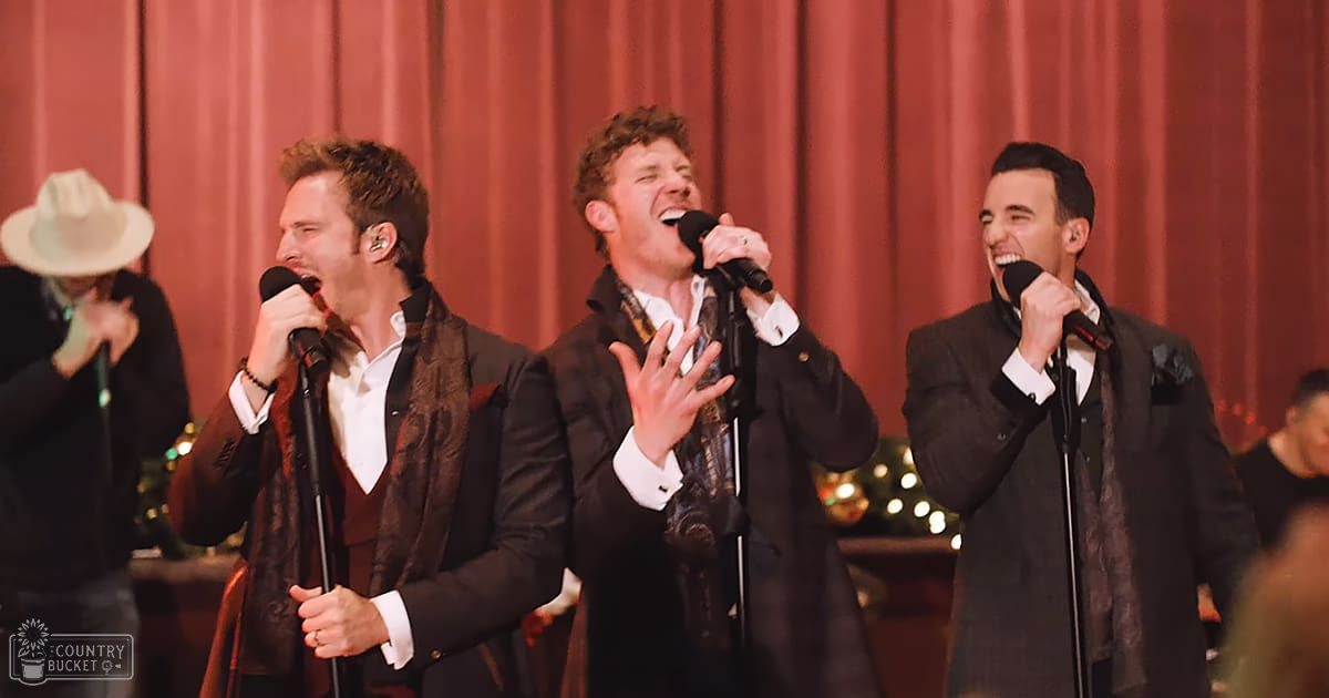 Group performance scene at an indoor event, possibly a concert or holiday celebration with formal attire and festive decor.