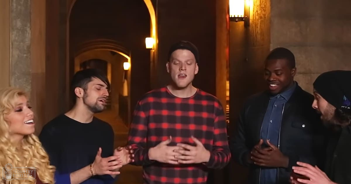 A group of individuals in an indoor hallway with stone walls and arched doorways, wearing various casual outfits under warm artificial lighting at evening time.