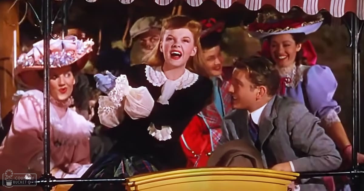 A woman in her young adult years wearing a black dress with white lace collar and cuffs, surrounded by other individuals dressed in period-appropriate attire at an amusement park ride. The setting suggests a festive or themed environment with decorative elements like striped awnings.