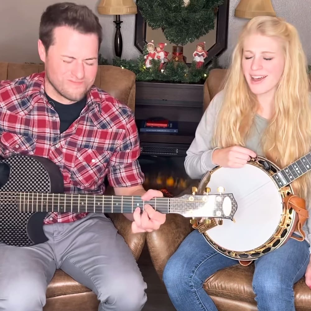 A young couple playing music together in a cozy living room decorated for Christmas.