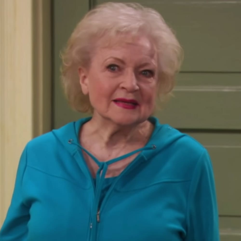 An older adult female in a relaxed, comfortable teal blue hoodie with a drawstring neckline and front zipper, indoors in a home setting.