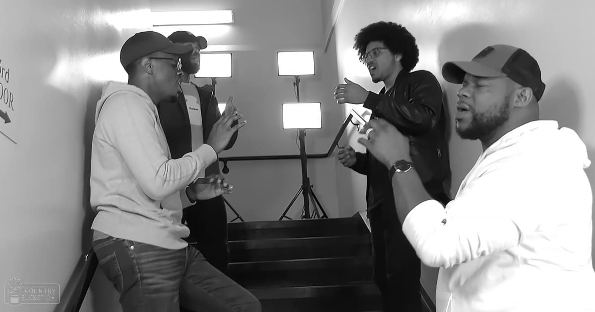 Young adults gathered indoors near a staircase with professional lighting equipment, wearing casual attire.