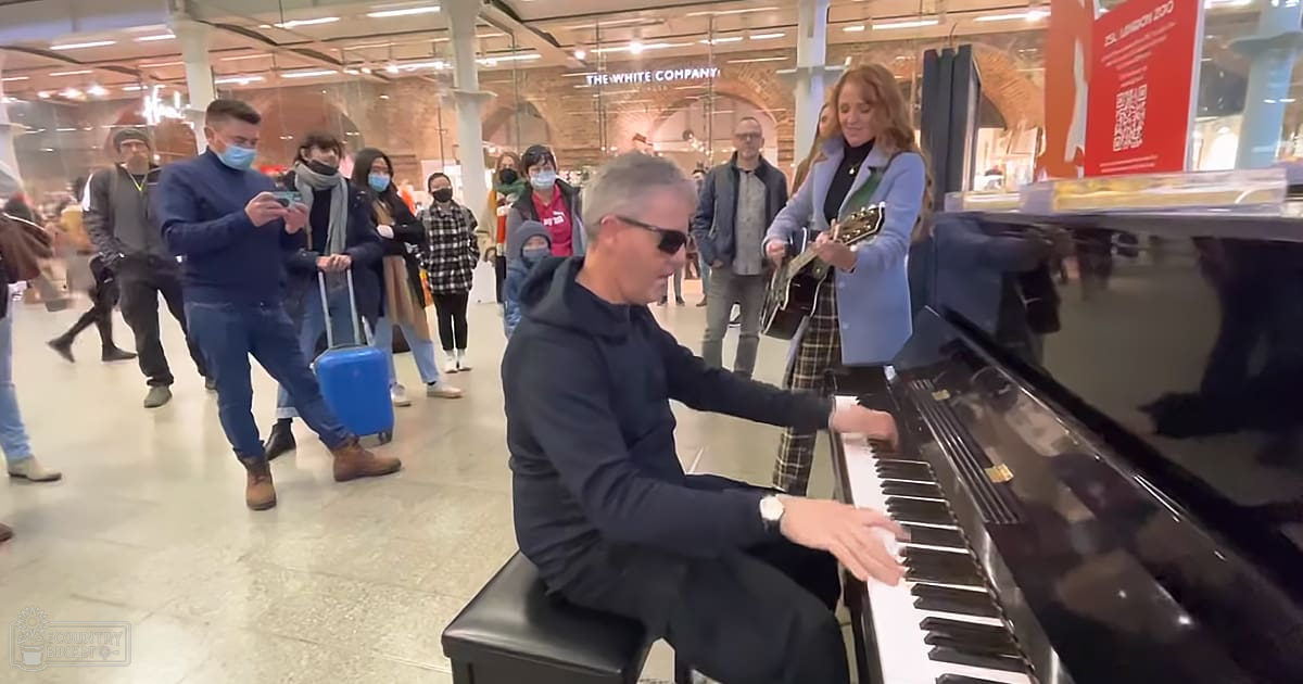 Man playing piano wearing dark sunglasses and hoodie, public space with signage for The White Company.