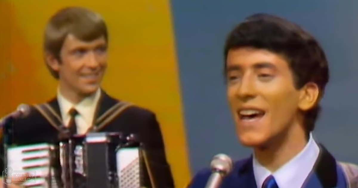 A musical performance scene with two young adult men, both wearing formal suits from the mid-20th century, performing under bright stage lighting against a yellow and blue backdrop.
