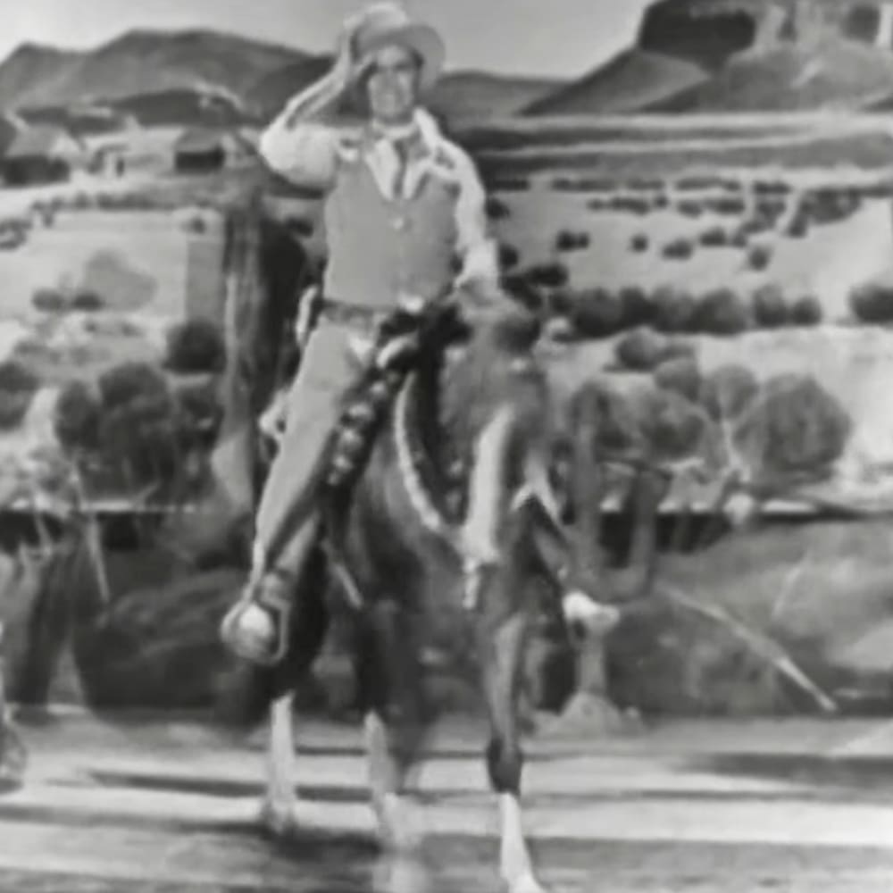 A cowboy riding a horse in a desert landscape with rocky terrain under natural daylight.