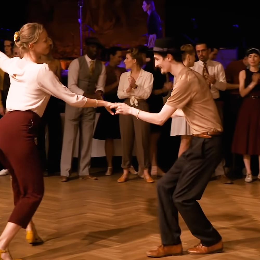 A couple dancing in an indoor social dance setting with dim, warm lighting.