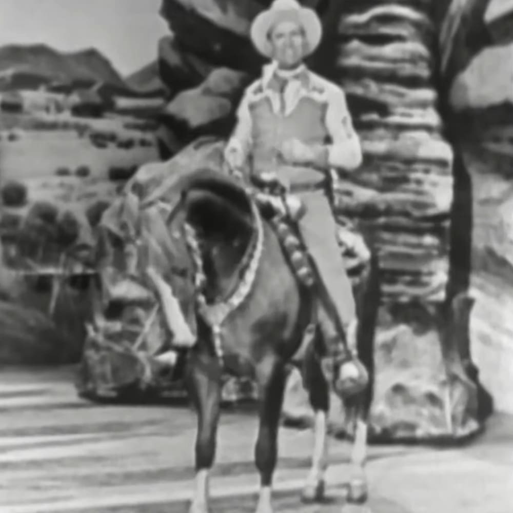A cowboy on horseback in a Western setting with rocky landscape and sunny day.