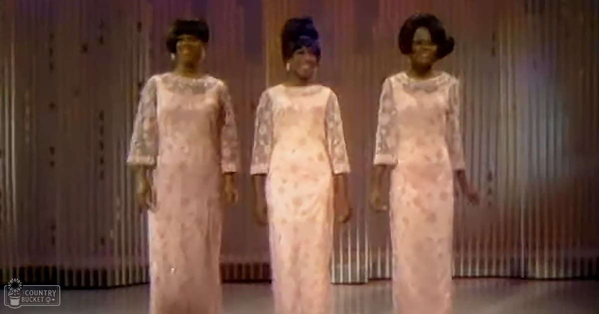 Three adult female performers in a studio setting, each wearing an elegant long gown with lace detailing and floral patterns.