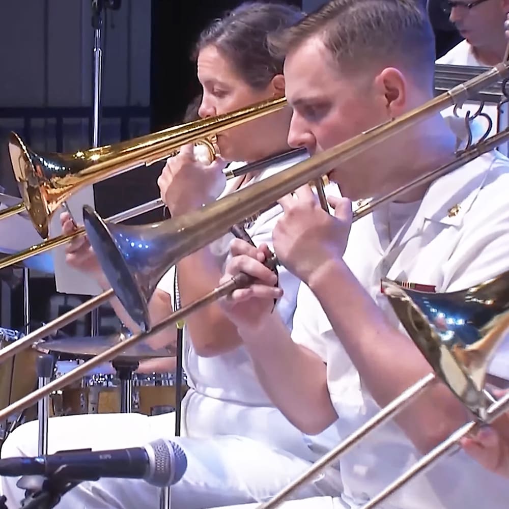 A musical performance with brass trombones, a microphone stand, and a drum set in an indoor stage or rehearsal space under artificial lighting.