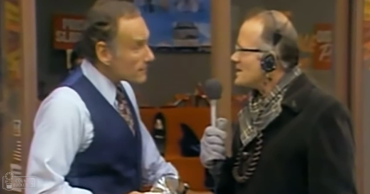 An adult male interviewer and guest in a mid-20th century interview setting with natural light, possibly daytime.