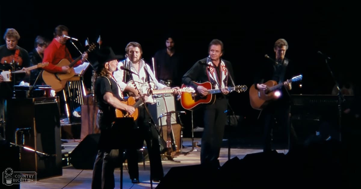 An indoor concert with multiple musicians performing, with various stage equipment and musical instruments under dim stage lighting.