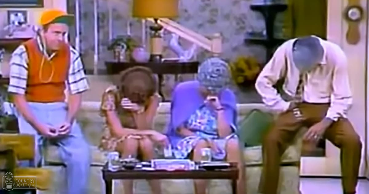A family scene indoors, likely a living room, with adults and children interacting in casual attire.