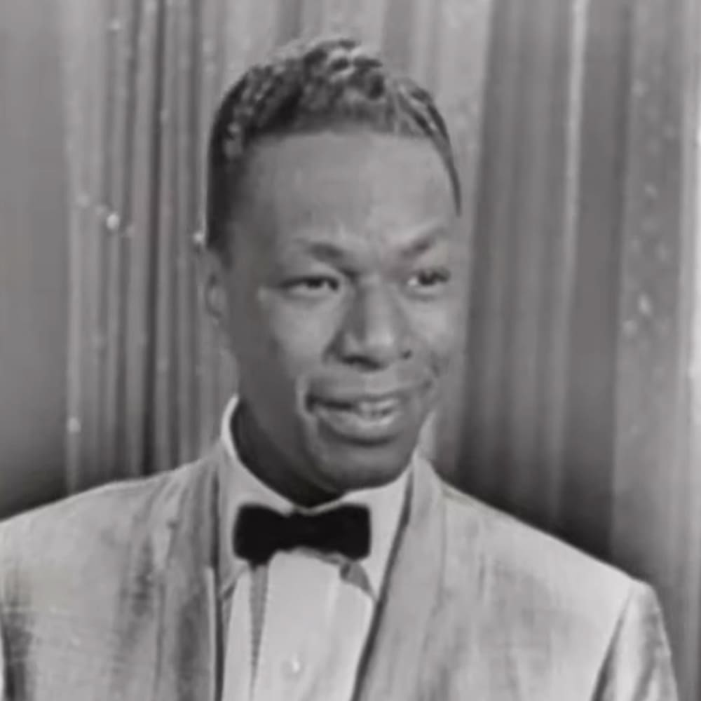 Young adult male in a tailored suit jacket with a bow tie against a backdrop of indoor curtains.