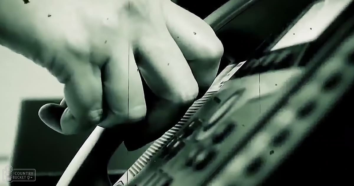 A hand gripping a semi-automatic rifle with textured grip, held indoors under dim lighting.