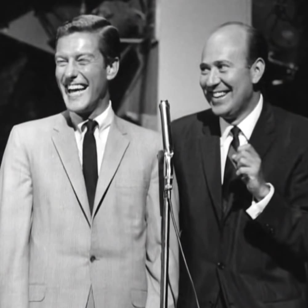 Two adult males wearing mid-20th century formal attire in a recording studio setting with professional equipment visible behind them.