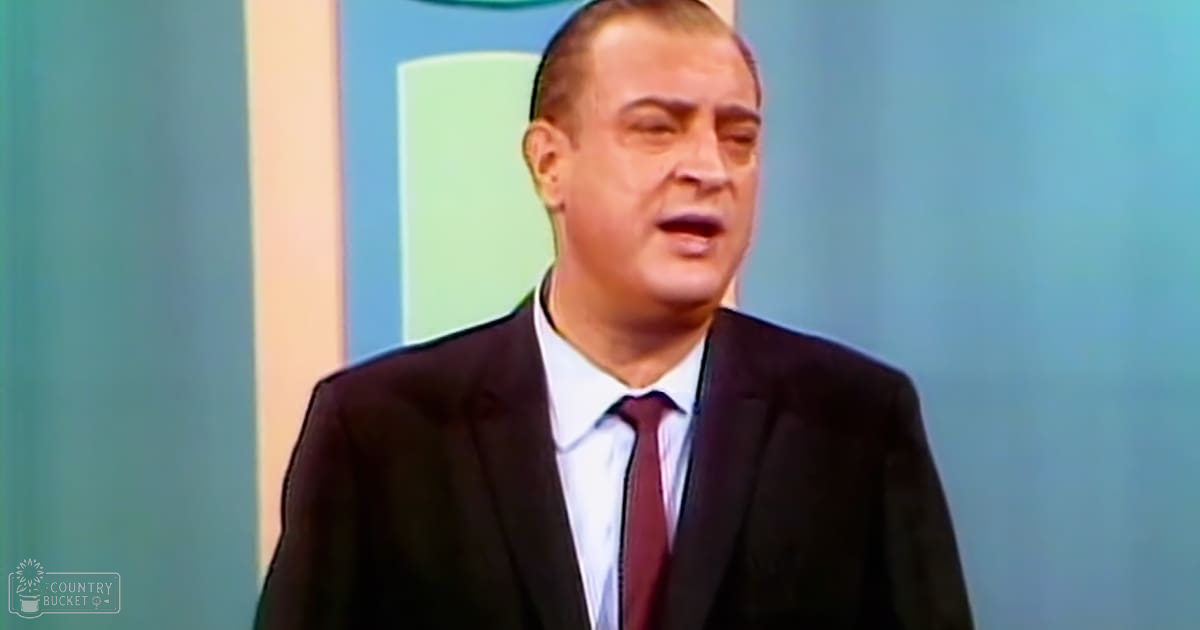A middle-aged man in a dark suit jacket, white dress shirt, and maroon tie stands indoors with a professional backdrop.