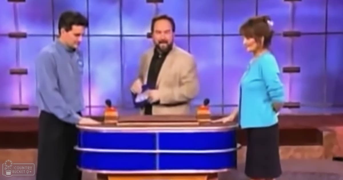 A television studio set with three adults, one possibly hosting or moderating a show, surrounded by professional equipment and backdrop elements typical of daytime broadcast settings.