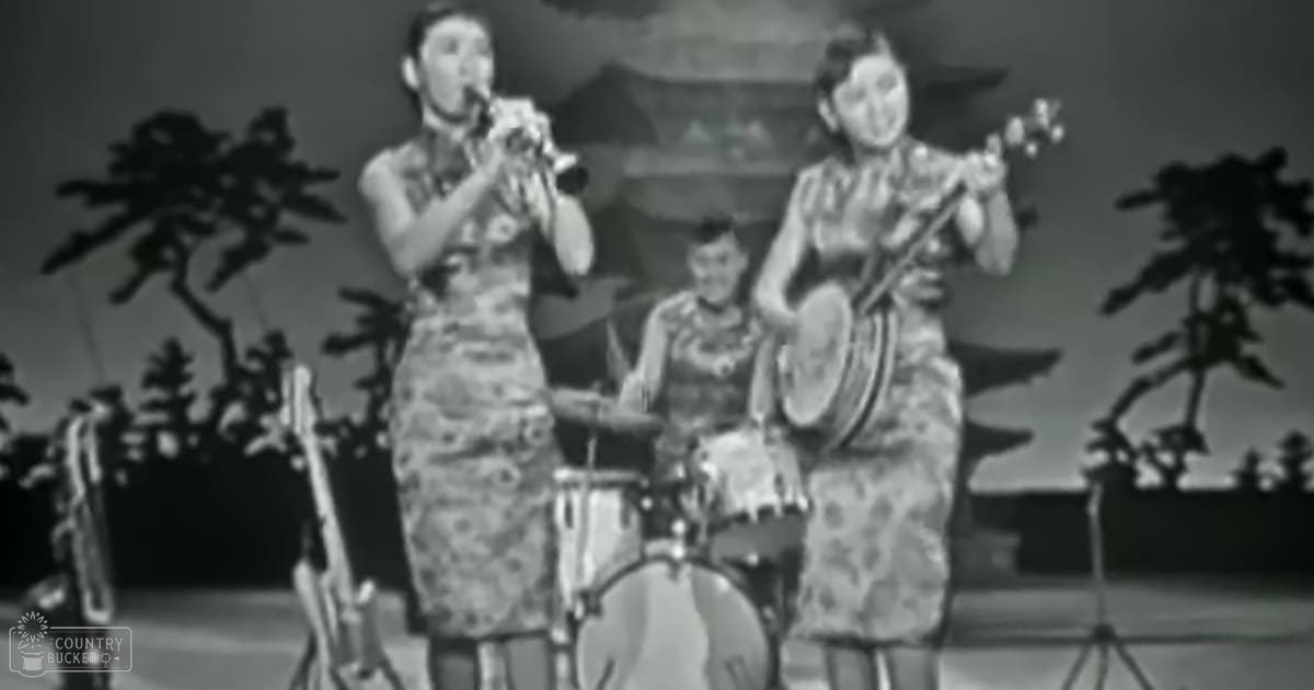 A musical performance with young adult females wearing floral-patterned dresses on a stage set against traditional Chinese-style decor in an indoor setting.