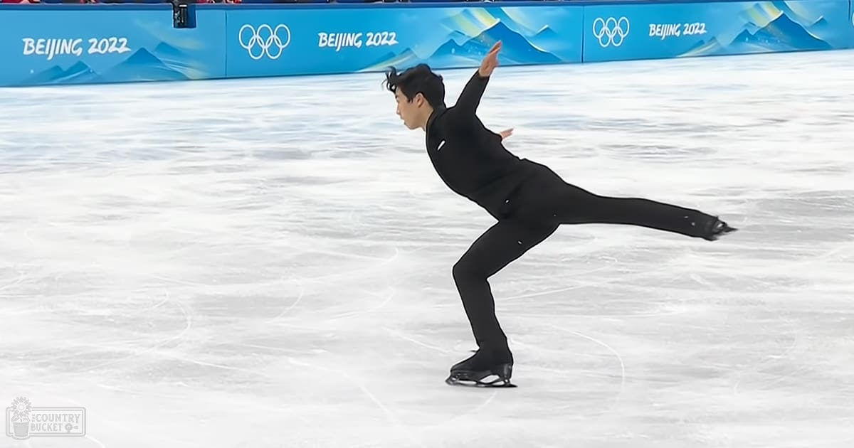 A male figure skater in a black long-sleeve skating outfit performs at an indoor ice rink during the Beijing 2022 Winter Olympics.