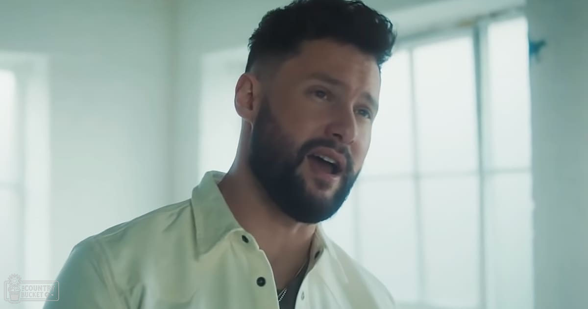 A young adult male in a relaxed fit light green button-up shirt with large windows allowing natural light into an indoor setting.