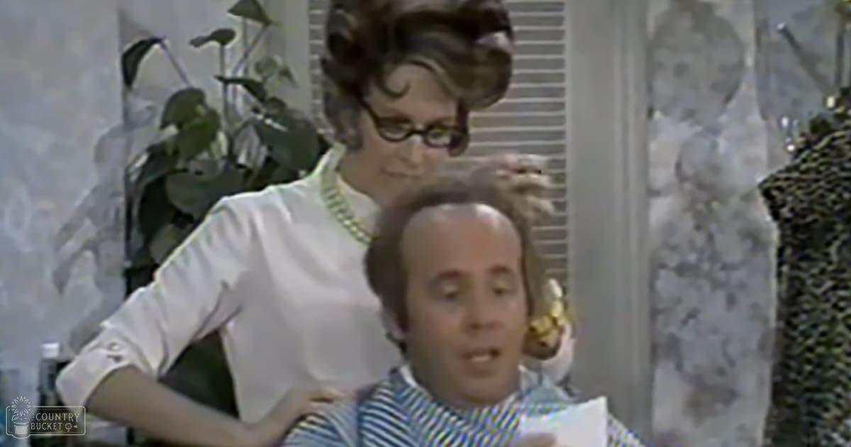 A woman styling another person's hair in a salon setting, wearing a white blouse with ruffled cuffs and a gold necklace.