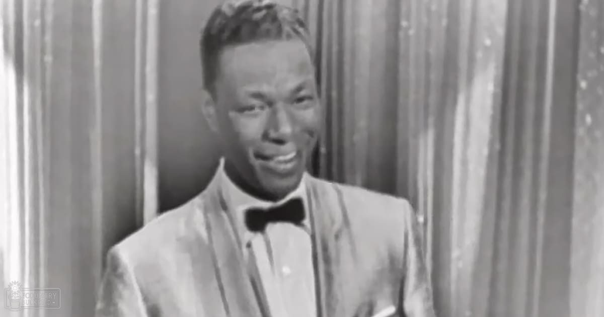 Young adult male in a formal suit jacket with lapels, collared shirt, and black bow tie against an indoor backdrop with vertical blinds or curtains.