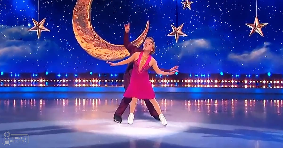 A figure skating pair performing on an ice rink against a starry night sky backdrop with decorative lighting, set during an evening performance under artificial moonlight and starlight.