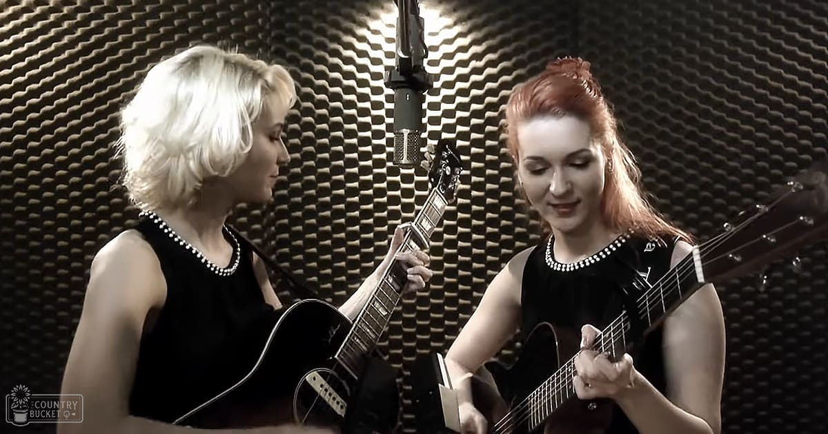Two young adult women in a recording studio, wearing sleeveless black dresses with pearl necklaces, performing music. Acoustic foam panels line the walls, and warm indoor lighting illuminates them.