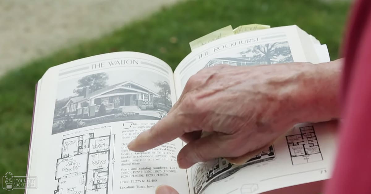An older adult reading 'The Walton' catalog outdoors in Tama, Iowa during late afternoon with soft lighting.