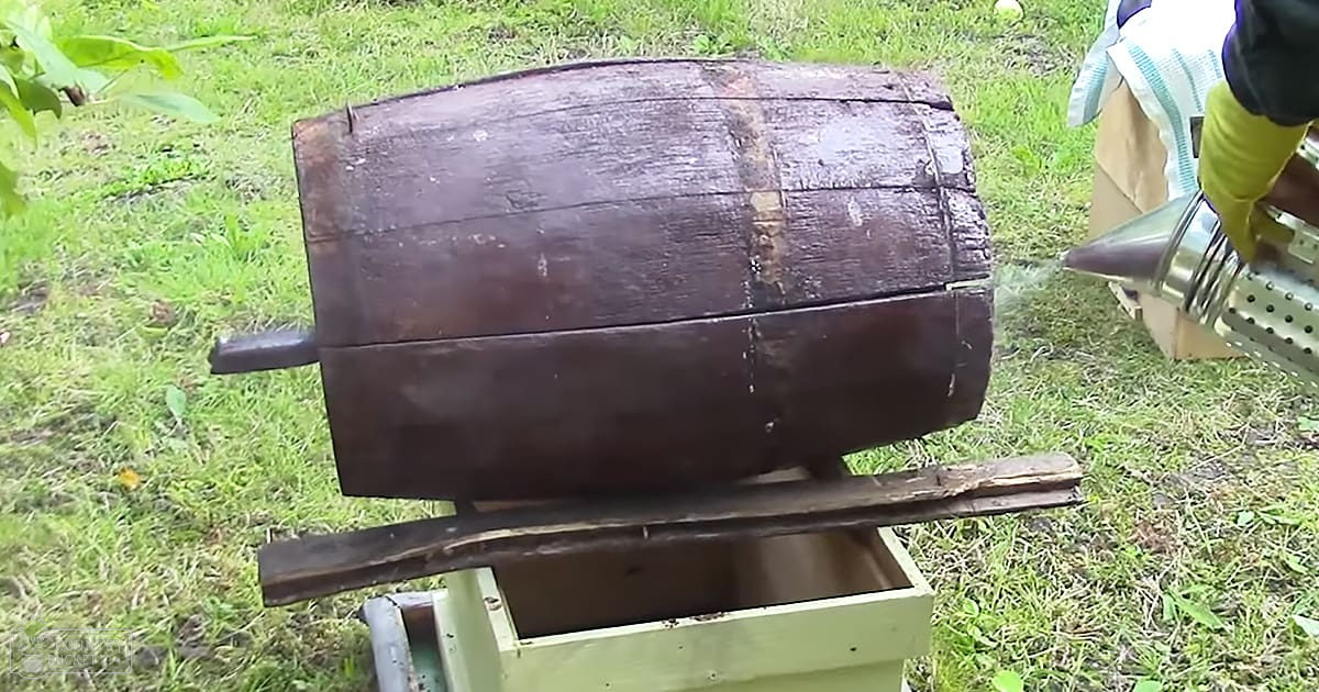A wooden barrel being cleaned with a pressure washer outdoors on a grassy area, daytime lighting.