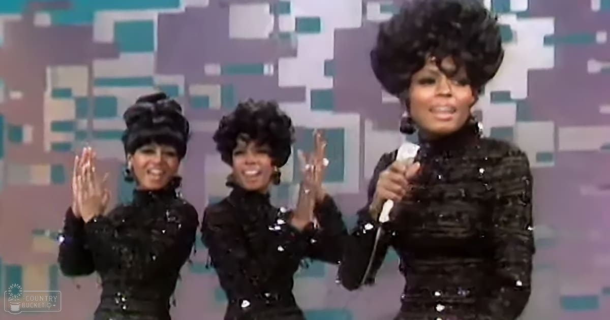 Musical performance with three adult female performers in black sequined tops, holding microphones on a stage with geometric purple and teal backdrop.