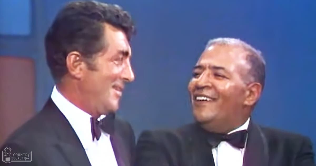 Two middle-aged adult males in a studio setting, dressed in formal attire from the mid-20th century style with dark suits and white dress shirts.