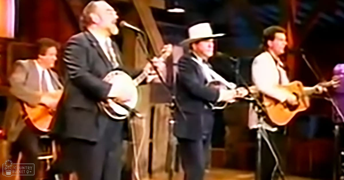A musical performance indoors with microphones on stands, a curtain backdrop, and musicians in formal attire playing banjos and an acoustic guitar.