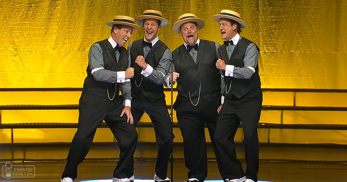 Group performance scene on a stage with performers wearing similar outfits, yellow lighting, indoor setting during evening.
