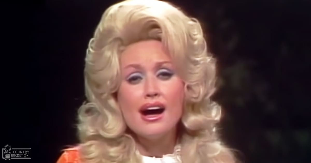 An adult female performer in a theatrical setting, wearing an orange and white formal dress with ruffled details under stage lighting.