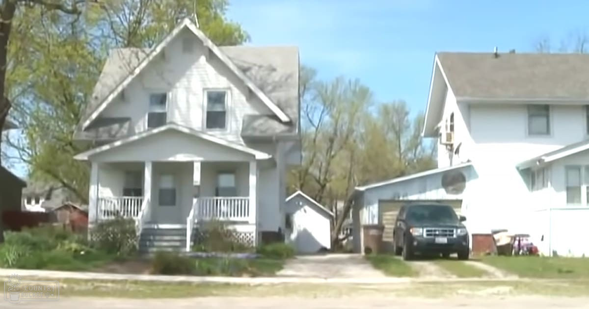 A serene suburban neighborhood scene with a clear blue sky, lush green trees, white houses, and a parked SUV on a sunny spring or summer day.