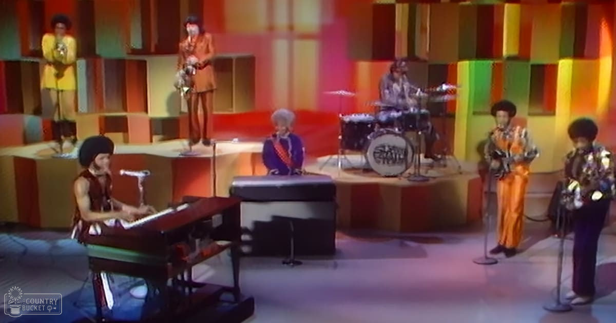 A musical performance from the 1970s on a stage with colorful geometric backdrops and performers in vibrant costumes.