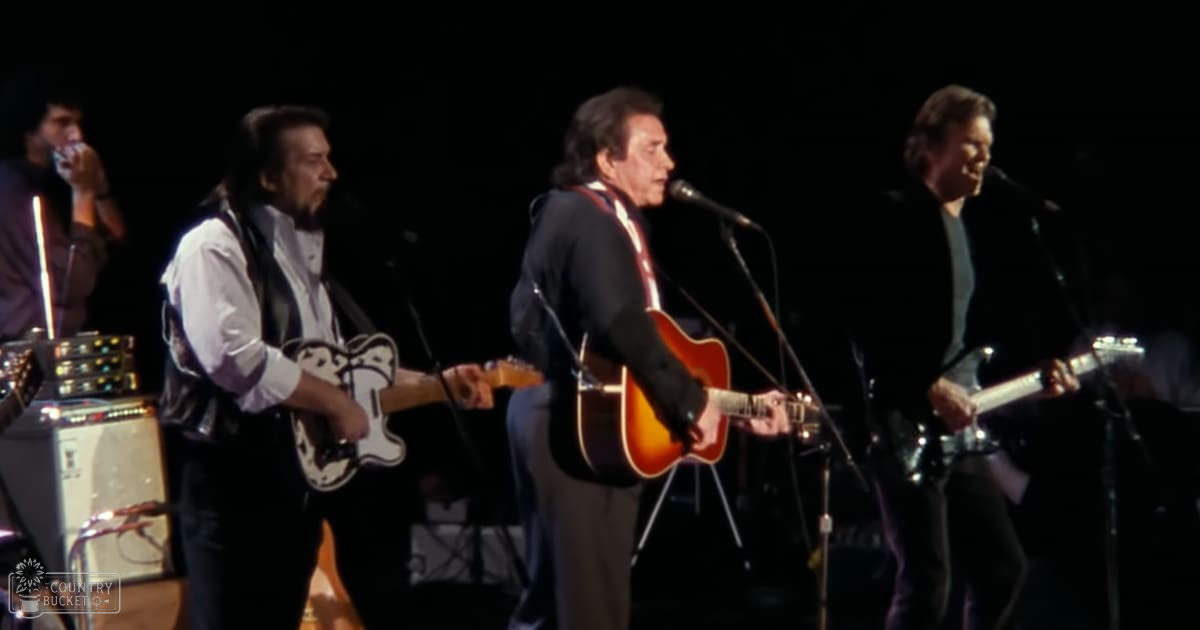 Musical performance by three adult males with microphones on stage in an indoor concert venue under dim lighting.