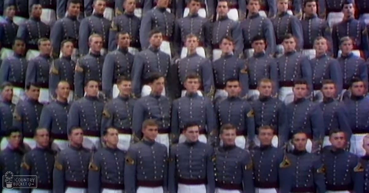 A group photo of young adult males in dark blue military-style uniforms outdoors on a sunny day with white seats and rows of bleachers.