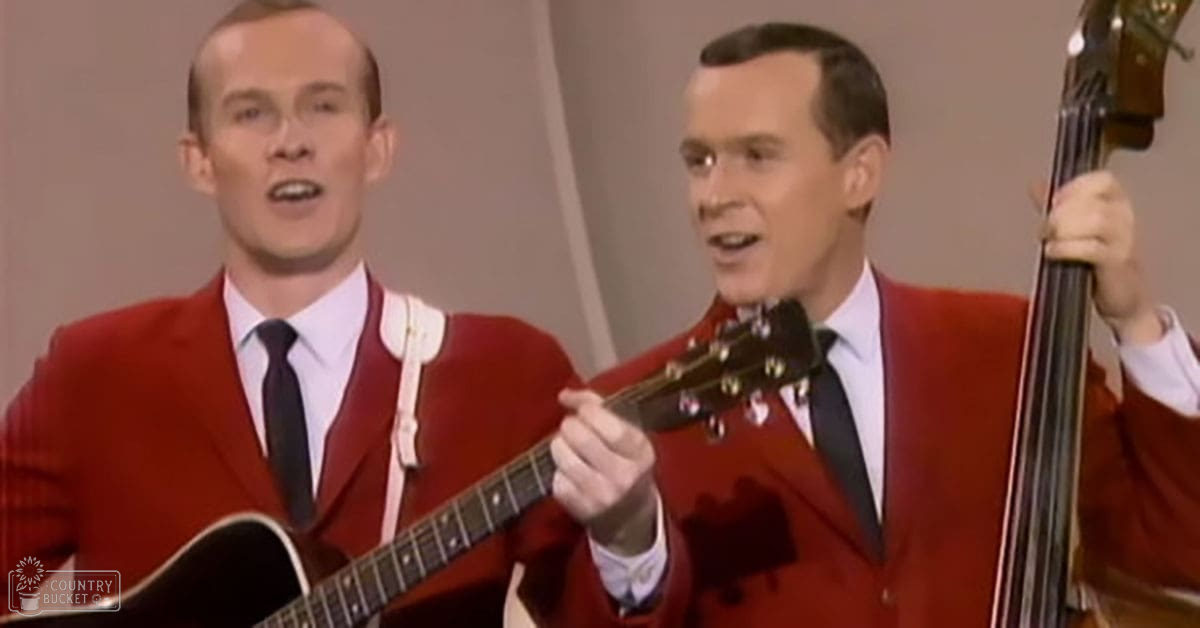 A musical performance scene with two young adult males in red blazers, white shirts, and dark ties. A guitar is held by one individual while the other holds a double bass.